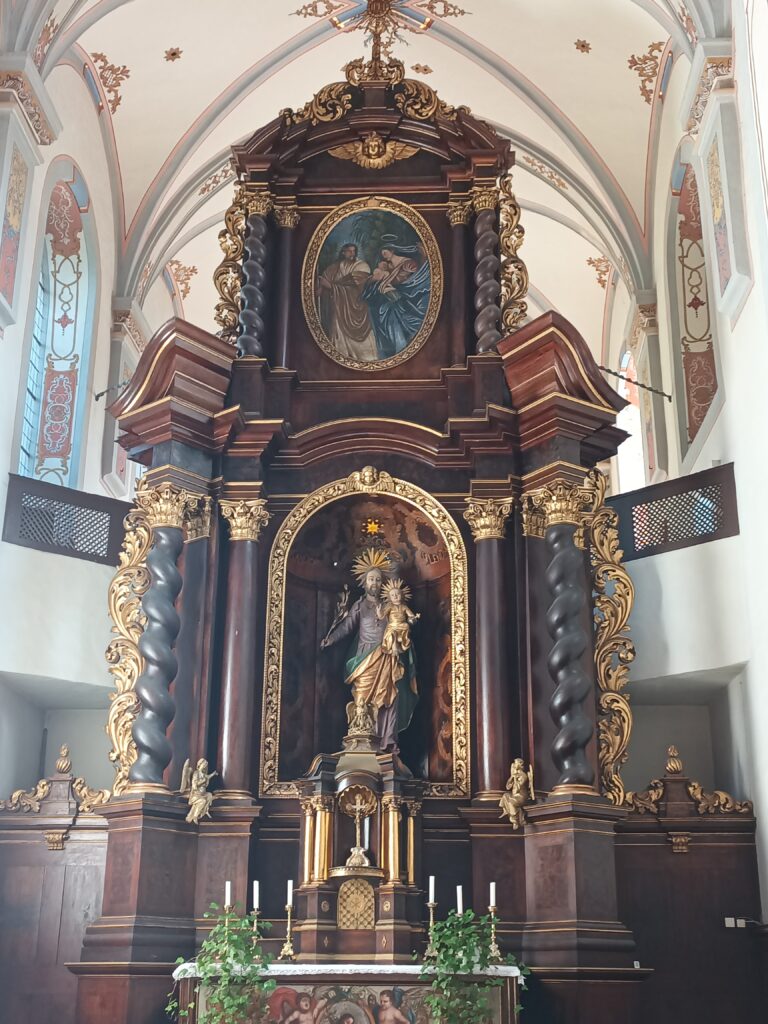 Blick auf den Hochaltar mit aus Nussbaumholz mit der Skulptur des Heiligen Josef. Dieser hält das Christuskind auf dem Arm. 