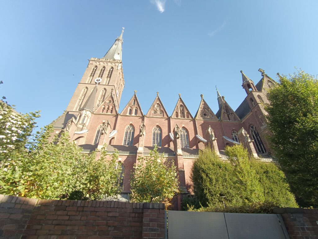 Seitliche Ansicht der St. Cornelius Kirche in Dülken, eingefasst von grünen Bäumen und einem klaren Himmel.