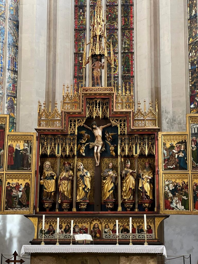 Detailansicht des geöffneten Zwölf-Boten-Altars in der St. Jakobskirche, mit geschnitzten Figuren und bemalten Flügeln.Diese Aufnahme zeigt eine Detailansicht des geöffneten Zwölf-Boten-Altars. Im Zentrum steht der geschnitzte Kreuzigungsschrein, flankiert von den Figuren der Apostel und Heiligen. Die Flügeltafeln sind reich bemalt und zeigen Szenen aus dem Leben Christi und Mariens.