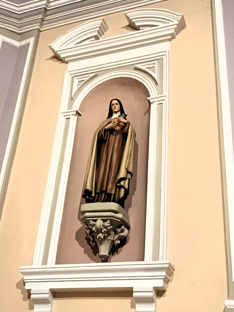 Statue der Heiligen Thérèse von Lisieux mit Rosen in einer Nische der Apsis der Kirche