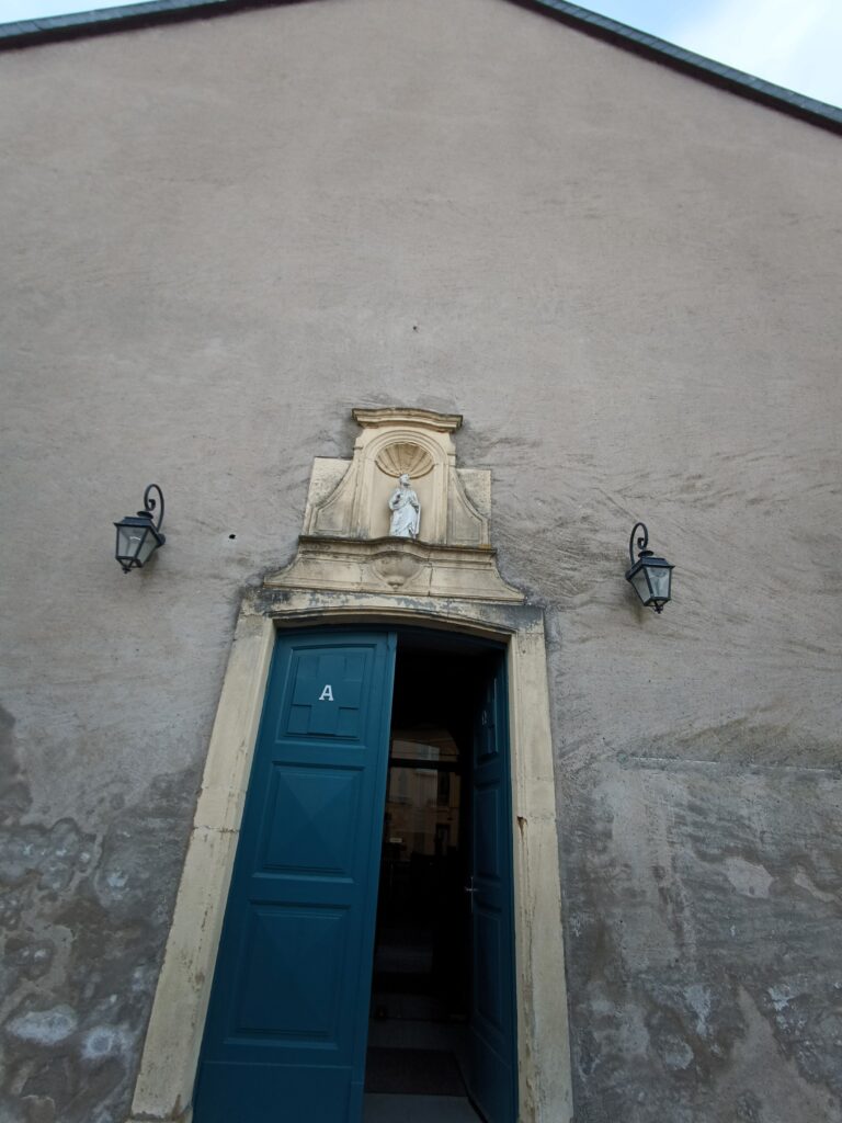 Das Kirchenportal der Église St Rémy mit markanten blauen Türen und Heiligenfigur.